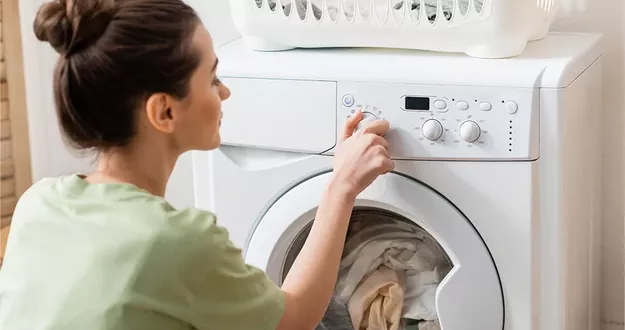 Eine junge Frau stellt das Programm ihrer Waschmaschine ein. Die Maschine ist gefüllt und bereit zum Waschen.